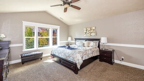 A bedroom with a bed, a nightstand, a bench, a ceiling fan, and a window with a view of trees. - Separation Canyon Retreat (Flagstaff)