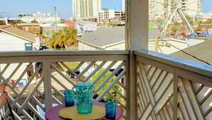 A balcony with a table and chairs, overlooking a cityscape with buildings and a Ferris wheel. - Across the street from the beach and a block from Mainstreet (North Myrtle Beach)