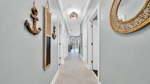 A hallway with light blue walls, a wooden anchor decoration, a mirror with ornate frame, and a ceiling light fixture.