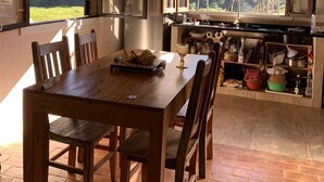 A rustic kitchen with a wooden table and chairs, a hanging light fixture, and a view of the outdoors through open windows. - Lots of charm and comfort in the mountains of Cunha (Cunha, Sp)