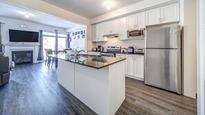 A modern kitchen with white cabinets, a stainless steel refrigerator, a built-in oven, and a flat-screen TV above the fireplace. - Executive Town Home - Historical Snowbridge Village, Mountain View Blue mountain (The Blue Mountains)