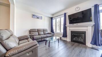 Een woonkamer met een leren bank, een glazen salontafel, een open haard en een flatscreen televisie.