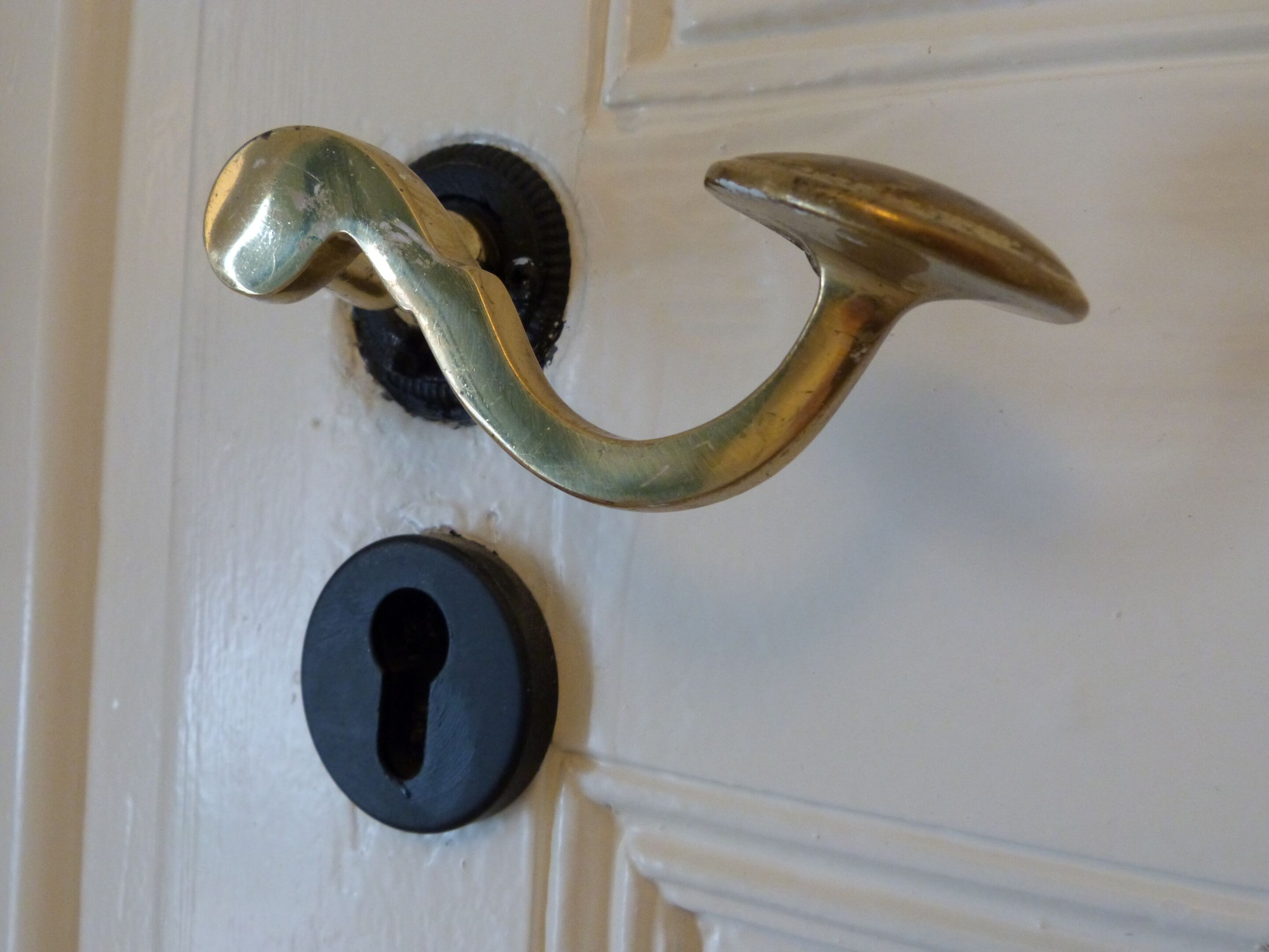 A brass door handle and a keyhole on a white door.