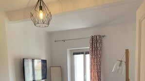 A modern living room with a sofa, a TV, a large mirror, and a geometric light fixture.