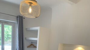 A bedroom with a bed, a chair, a bedside table, a lamp, and a window with curtains.