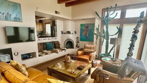 A living room with a sofa, armchairs, a coffee table, a fireplace, a television, and a large cactus plant. - Spectacular Mountain Views, Supreme Tranquility & Privacy in Tesuque! (Santa Fe)