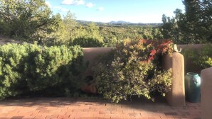 A patio with a brick floor, surrounded by dense greenery and a view of distant mountains. - Spectacular Mountain Views, Supreme Tranquility & Privacy in Tesuque! (Santa Fe)