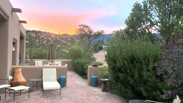 An outdoor patio with brick flooring, white chairs, a table, and a large urn. - Spectacular Mountain Views, Supreme Tranquility & Privacy in Tesuque! (Santa Fe)