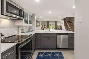 A modern kitchen with a dishwasher, stove, microwave, and a large island with a sink.