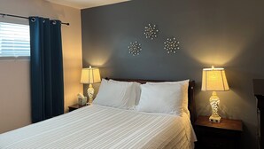 Een net opgemaakt bed met witte lakens, twee bedlampjes en decoratieve wandkunst.