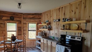 Cocina de cabaña de madera con una mesa de comedor, sillas, estufa y repisas con vajilla.