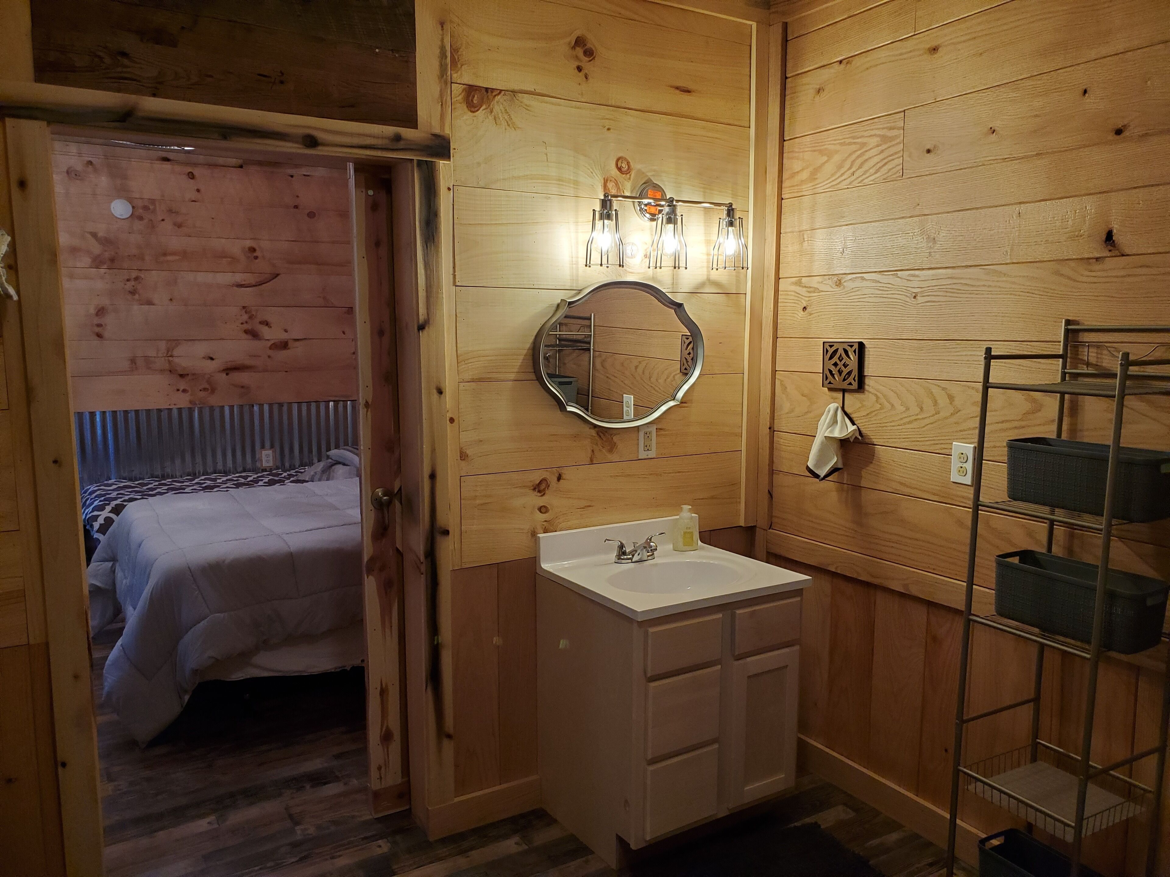 A wooden-paneled room with a bed, a white sink, a mirror, and a shelf with storage boxes.