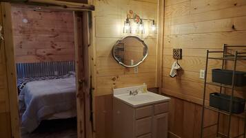 A wooden-paneled room with a bed, a white sink, a mirror, and a shelf with storage boxes.