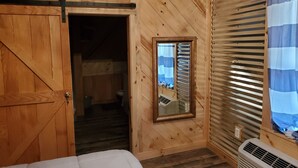 Una habitación de madera con una cama, un espejo y una ventana con persianas.