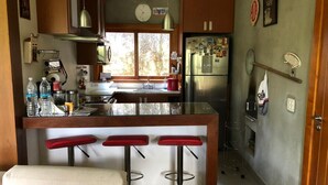 A kitchen with a central island, bar stools, a refrigerator, and a clock on the wall. - Retreat with Suite in a Secure Condominium | Nature and Stunning Views  (RJ)