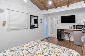 A bedroom with a bed, a desk, a chair, a TV, and a bathroom.
