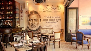 L’intérieur d’un restaurant, avec une grande fresque murale, des meubles en bois et un coin bar où sont exposées des bouteilles.