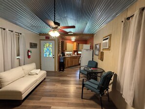 A room with a sofa, a table with chairs, a kitchen area in the background, and a ceiling fan. -  Private Oasis at Jenny's cabin (New Braunfels)