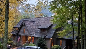 A rustic cabin with a steeply pitched roof, a porch with a railing, and a flag in front.