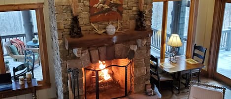 A cozy living room with a stone fireplace, comfortable seating, and a view through large windows.