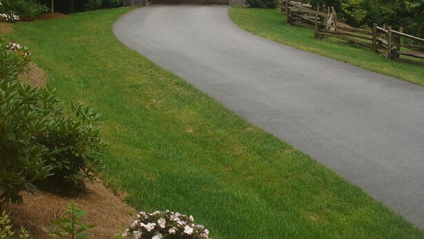 A wooden covered bridge in a lush, green landscape with a paved road leading through it.