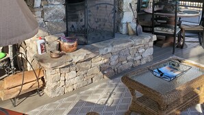 A stone fireplace with a log shelf, wicker furniture, and a view of the outdoors.