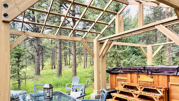 A wooden structure with a glass table and chairs, surrounded by a forest.