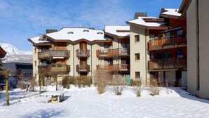 A multi-story hotel with balconies, a snow-covered courtyard, and a mountain in the background. - Apartment Allmi by Interhome (Meiringen)