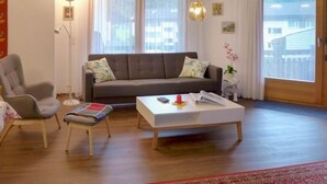 A living room with a grey sofa, a white coffee table, a grey armchair, and a red and white patterned rug. - Apartment Allmi by Interhome (Meiringen)