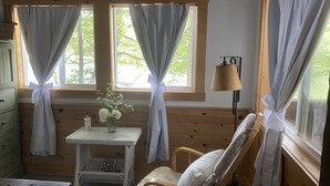 A cozy room with wooden walls and a bed with white bedding. There is a small table with a vase of flowers and a lamp. - Lakeside home. Fishing, paddle boarding, swimming, and easy lake  fun.  (Warner)