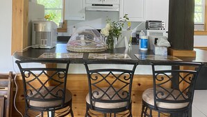 A kitchen with a central island, three bar stools, white cabinets, and a window with greenery outside. - Lakeside home. Fishing, paddle boarding, swimming, and easy lake  fun.  (Warner)