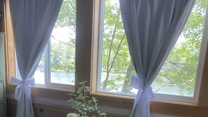 A room with a bed, a small table with a vase of flowers, and a window with curtains tied back. - Lakeside home. Fishing, paddle boarding, swimming, and easy lake  fun.  (Warner)