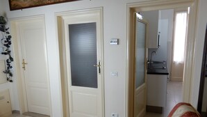 Um quarto com duas portas, uma delas com grade de metal, uma tomada e um interruptor de luz. Um sofá vermelho está em primeiro plano.