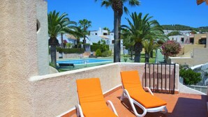 A rooftop terrace with two lounge chairs and a pool in the background.