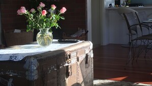 A rustic kitchen with a wooden table, a vase of pink roses, and a vintage suitcase. - Spacious house with optimal decks near popular  beaches (Warkworth)