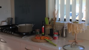 A kitchen with a stove, pots, a cutting board with vegetables, and various kitchen items on the counter. - Spacious house with optimal decks near popular  beaches (Warkworth)