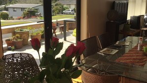 A dining area with a glass table, wicker chairs, a vase with flowers, and a view of the outside. - Spacious house with optimal decks near popular  beaches (Warkworth)