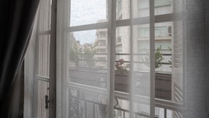 A view through a window with a grid pattern, revealing a street and buildings in the background. - Polytimon, an Athenian Neoclassical Apartment (Athens)
