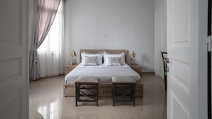 A bedroom with a bed, two bedside tables, a nightstand, a window with curtains, and a door. - Polytimon, an Athenian Neoclassical Apartment (Athens)