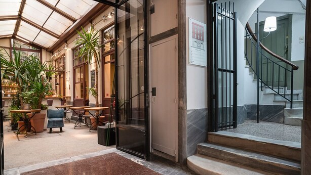 A spacious indoor area with a glass door entrance, a staircase with a railing, and several tables and chairs arranged for seating. - Polytimon, an Athenian Neoclassical Apartment (Athens)