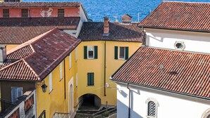 A narrow street with buildings featuring red-tiled roofs and a clear view of the water in the background.