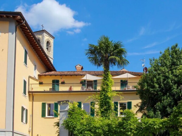 A yellow building with a bell tower, green shutters, and outdoor seating.