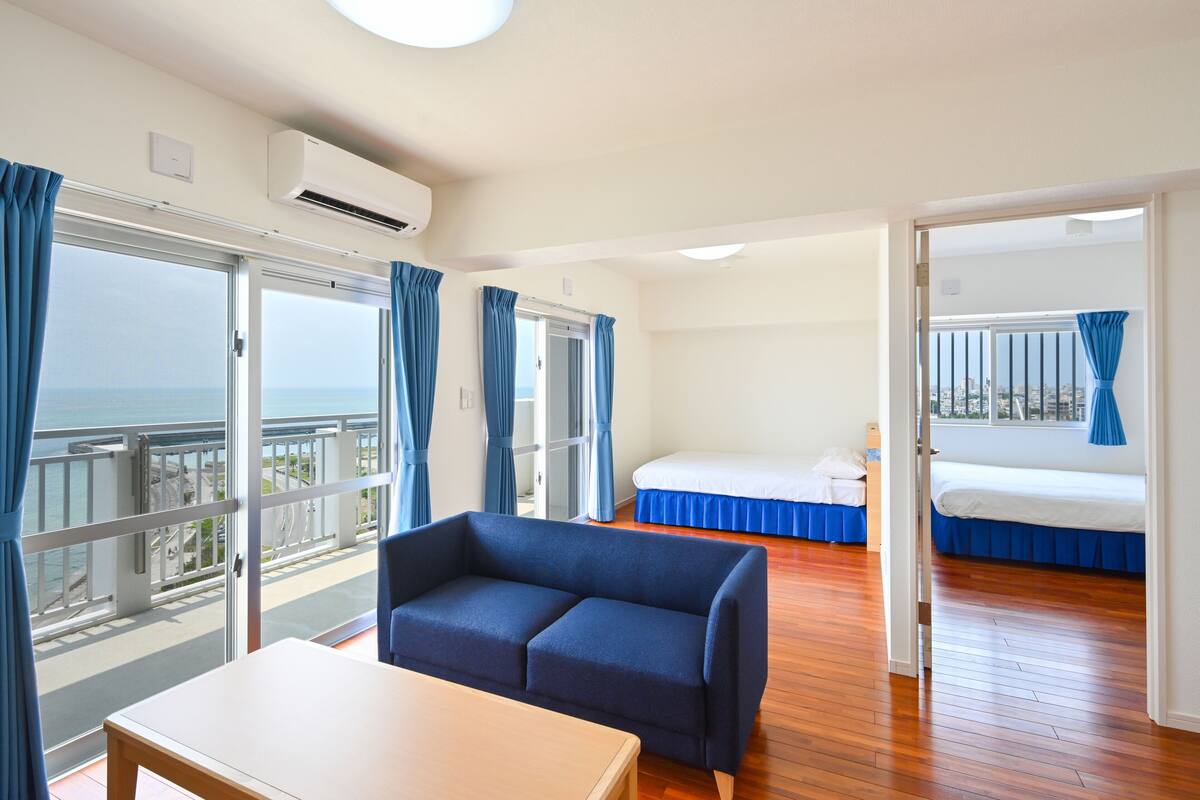 A hotel room with a balcony, a sofa, a bed, and a wooden floor.