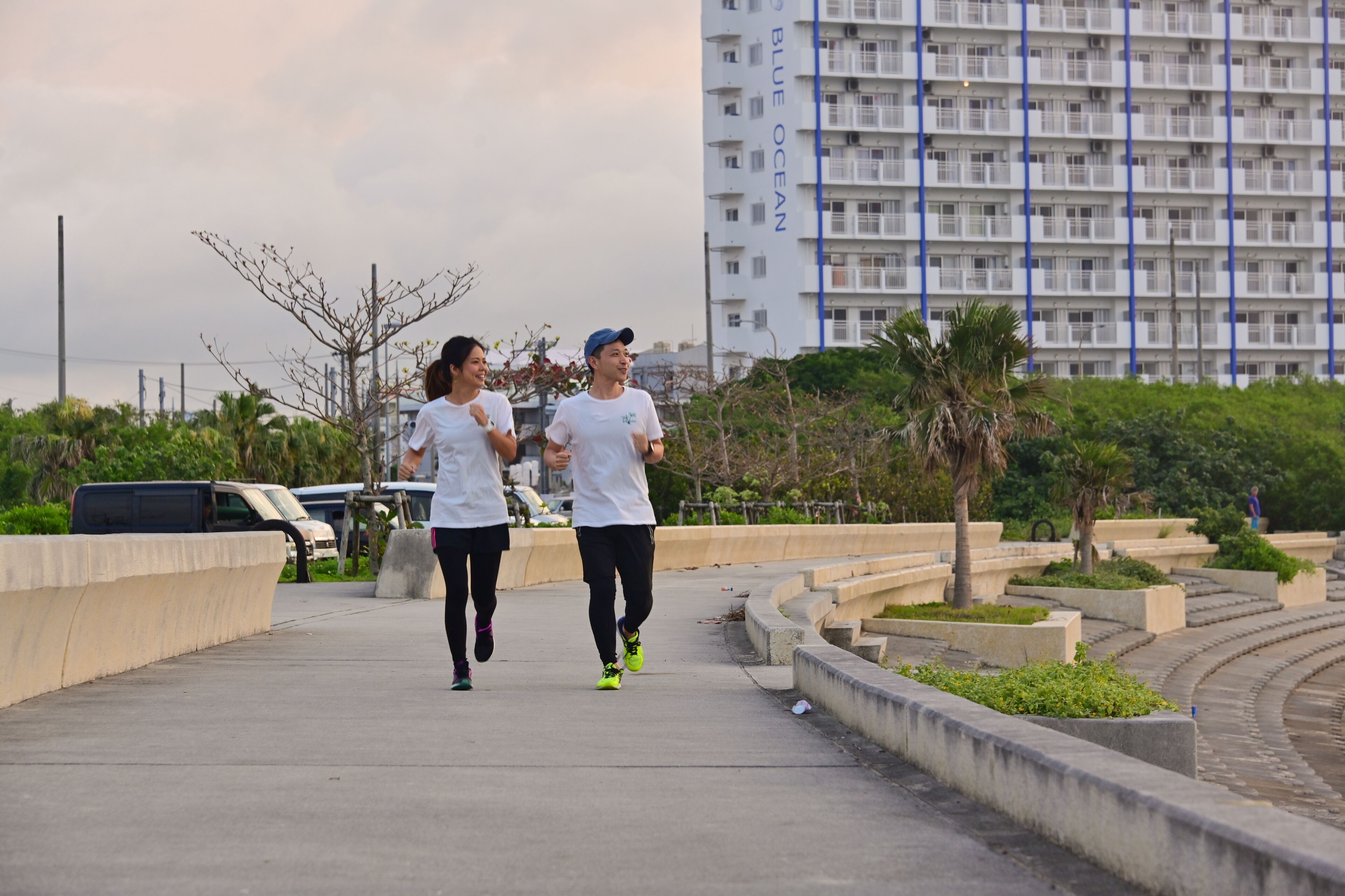 Two people jogging on a concrete path with a modern building in the background.