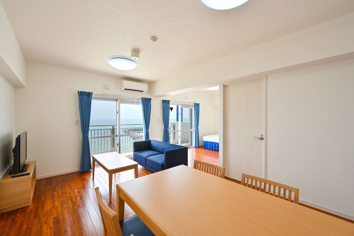 A room with a wooden floor, a sofa, a dining table, and a TV.