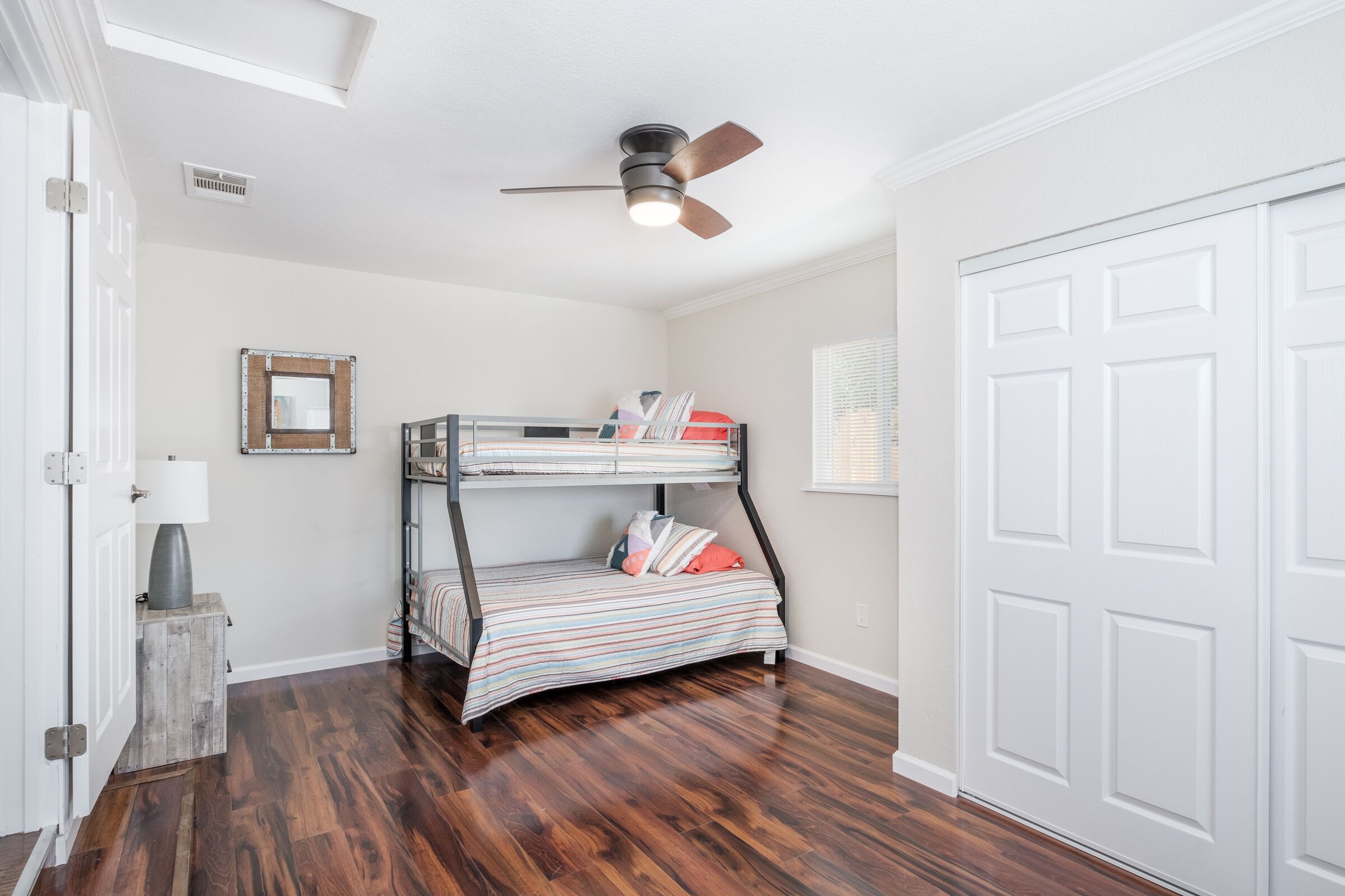 A room with a bunk bed, wooden flooring, a ceiling fan, and a white door.