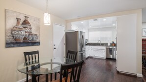 Una cocina moderna con armarios blancos, un refrigerador de acero inoxidable y un comedor con mesa de vidrio y sillas de madera.