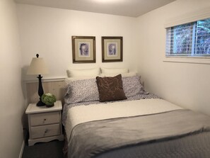 Una camera da letto con un letto, un comodino, una lampada, due quadri appesi al muro e una finestra con persiane.