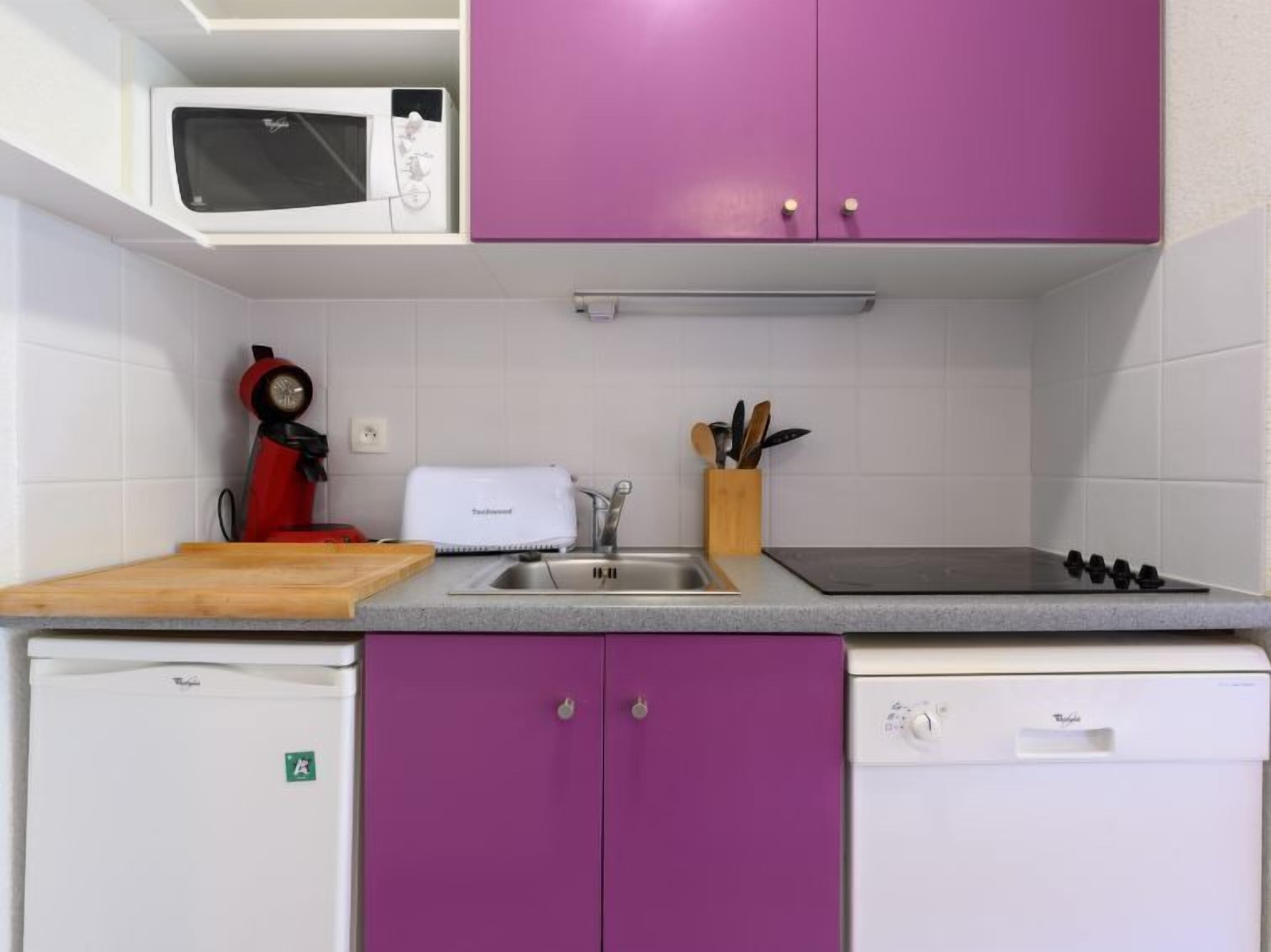 A compact kitchen with white cabinets, a microwave, a toaster, a sink, and a dishwasher.