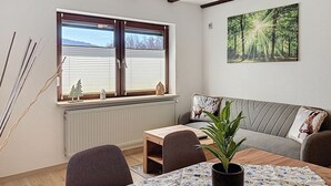 Una stanza accogliente con un'ampia finestra, un tavolo di legno, un divano e una pianta.